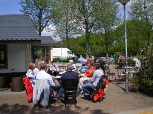 Camping de Zwammenberg في De Moer: مجموعة من الناس يجلسون على الطاولات في الحديقة