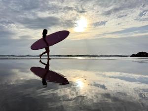 Una mujer caminando por la playa con una tabla de surf en Hotel NALU　ホテルナル, en Kannoura