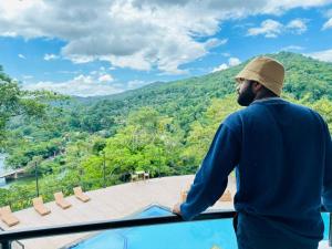 a man standing on a balcony looking out at the mountains at Indra Manel Family Holiday Resort Kandy in Kandy