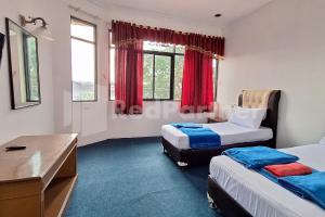 a bedroom with two beds and a desk and window at Hotel Graha Muslim RedPartner in Bukittinggi