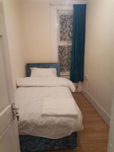a bedroom with a bed and a window with blue curtains at Nice Single Room near London Seven Kings Train station in London