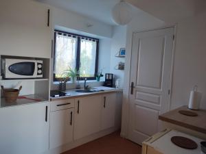 eine Küche mit weißen Schränken, einer Mikrowelle und einer Tür in der Unterkunft Gîte La Pâquerie in Le Louroux-Béconnais