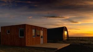 Cabaña de madera pequeña con puesta de sol en el fondo en Aurora Igloo, en Hella