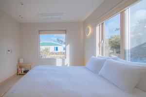 a bedroom with a white bed and a large window at Aewol Gilro in Jeju