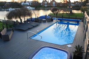 a large swimming pool with lounge chairs next to a river at Old Wharf Cottage - Riverside Living with Pool in Wraysbury
