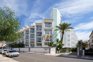 a tall white building with a palm tree in front of it at Aluasun Lago Rojo - Adults recommended in Torremolinos