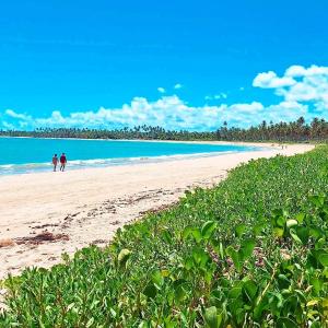 two people walking on a beach near the ocean at Arataba Hotel Boutique e Bistrô - 150 mts do mar in Pôrto de Pedras