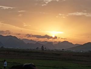 a sunset over a field with mountains in the background at Palafita Bungalow in Phong Nha