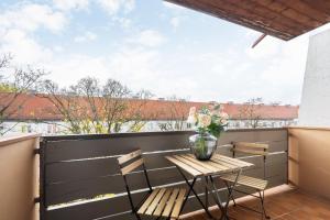 un balcón con mesa, sillas y un jarrón de flores en Homaris Apartments München Laim en Múnich