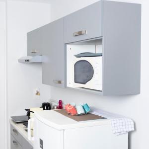 a white kitchen with a microwave and a white refrigerator at Hotel La Ciotat - A deux pas de l'eau in La Ciotat
