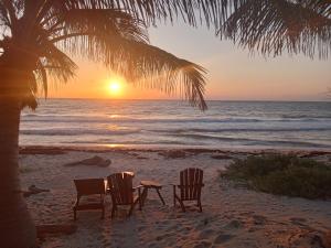two chairs and a table on the beach at sunset at Playa Lakin-ha beachfront cabins in Tulum