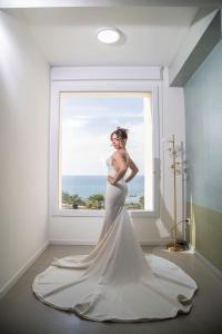 Una mujer con un vestido de novia parada frente a una ventana en Cocciu d’amuri en Terrasini Favarotta