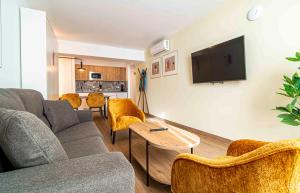 Una sala de estar con un sofá y sillas y un televisor. en Apartamentos 1 Abril, en Málaga