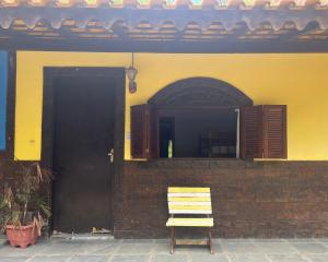 a yellow house with a wooden chair next to a door at Pesque pague pousada do Carlinho in Pinheiral