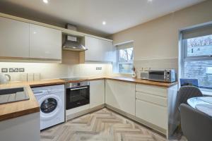 a kitchen with white cabinets and a washer and dryer at Host & Stay - Studio No.8 in Alnwick