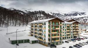 a large building in the snow with parked cars at Crystal Residence Apartment 224 in Bakuriani