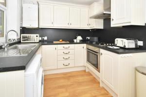 a white kitchen with white cabinets and black counter tops at Squirrel Cottage by YourStays in Stoke on Trent