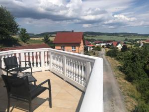 a balcony with two chairs and a view of a house at Ferienwohnung Graswald mit Panoramablick in die Rhön in Kaltennordheim