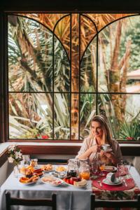 Vila Suzana Parque Hotel في كانيلا: امرأة تجلس على طاولة أمام النافذة