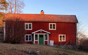 a red barn with a green door in a field at Flemma Gård The lake view with sauna in Vreta Kloster