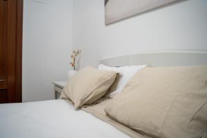 un letto con lenzuola e cuscini bianchi in una stanza di Bonito piso en San Ildefonso - Centro a Jaén