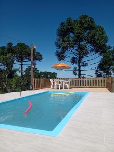 uma piscina com um guarda-sol, uma mesa e cadeiras em Casa aconchegante em meio a natureza em Caxias do Sul