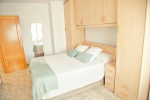 een kleine slaapkamer met een wit bed en houten kasten bij Apartamento Playa Xilxes in Xilxes