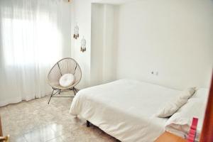 a white bedroom with a bed and a chair at Apartamento Playa Xilxes in Xilxes