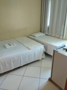 two beds in a room with white tile floors at Hotel Algaroba Anexo in Bom Jesus da Lapa