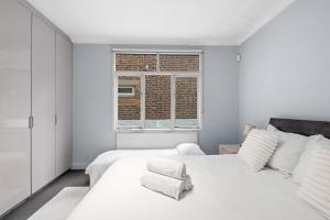 a white bedroom with a bed and a window at Londwell, Boutique Bliss Nestled in Knightsbridge by Harrods in London