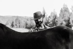 Ein Mann mit einem Cowboyhut, der neben einer Kuh steht. in der Unterkunft Ranch de Frisons le Fer à Cheval - Le Madison - Chalet Rustchic au pied du Mont Mégantic in La Patrie