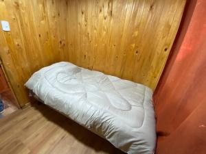 Cama pequeña en habitación con pared de madera en Cabaña en sector residencial, en Puerto Aysén