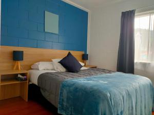 a bedroom with a bed with a blue wall at Aarangi Tui Motel in Paihia