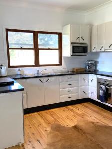 a kitchen with white cabinets and a wooden floor at Hannah's Place in the heart of Lovedale, Hunter Valley wine country, Free bottle of wine with each booking in Lovedale