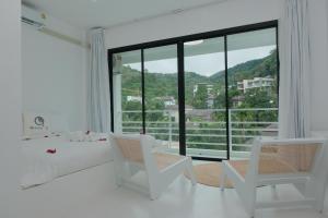 een witte kamer met een bed en stoelen en een groot raam bij MoonE in Ka Rorn