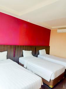 three beds in a room with a red wall at Hotel Grand Nanggroe in Banda Aceh