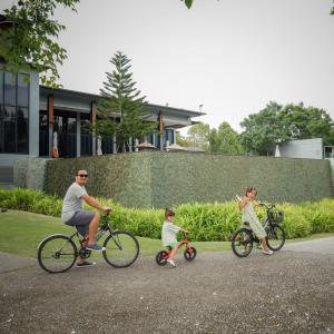 Un homme et deux enfants montent à vélo dans une rue dans l'établissement dusitD2 Khao Yai, à Mu Si