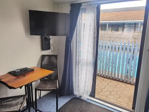 a room with a desk and a window with a table and chairs at Cortez Motel in Whakatane