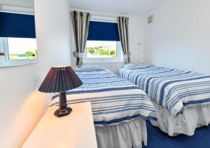 two beds in a room with a lamp and windows at 139 Cae Du in Abersoch