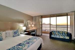 a hotel room with a bed and a desk and window at Lagoon Beach Hotel & Spa in Cape Town