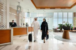 Delta Hotels by Marriott City Center Doha في الدوحة: رجل وامرأة يسيران في المطار مع حقيبة سفر