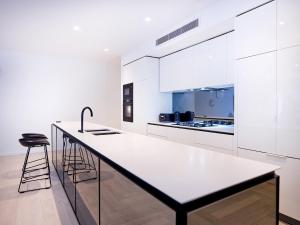a white kitchen with a large counter and stools at Palm Beach Lux Villa in Gold Coast