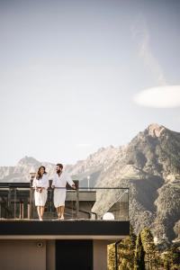 two women walking on a balcony with mountains in the background at Vinea - Apartments in Tirolo