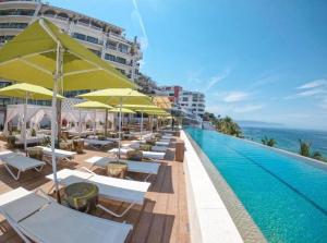 een zwembad met stoelen en parasols en de oceaan bij Grant's Studio at Mantamar Tower in Puerto Vallarta