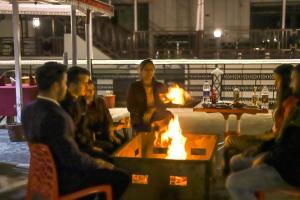 a group of people sitting around a fire pit at Hotel Varuni- On Mall Road, Mcleod Ganj, Dharamshala in Dharamshala