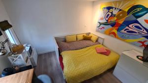 une petite chambre avec un lit jaune et une peinture murale dans l'établissement Le studio dans le jardin., à Rosny-sous-Bois