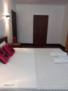 Amith Villa Kabalana في كوغالا: غرفة نوم بها سرير أبيض ومخدات حمراء