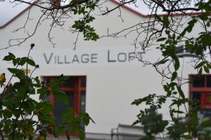a white building with a sign that reads village lodge at Village Loft in Sankt Stefan im Rosental