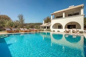 a swimming pool with chairs and a house at The Grove Villa in Velonádes