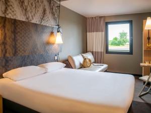 una habitación de hotel con una gran cama blanca y una silla en ibis Pontorson Baie Du Mont Saint Michel, en Saint-Georges-de-Gréhaigne